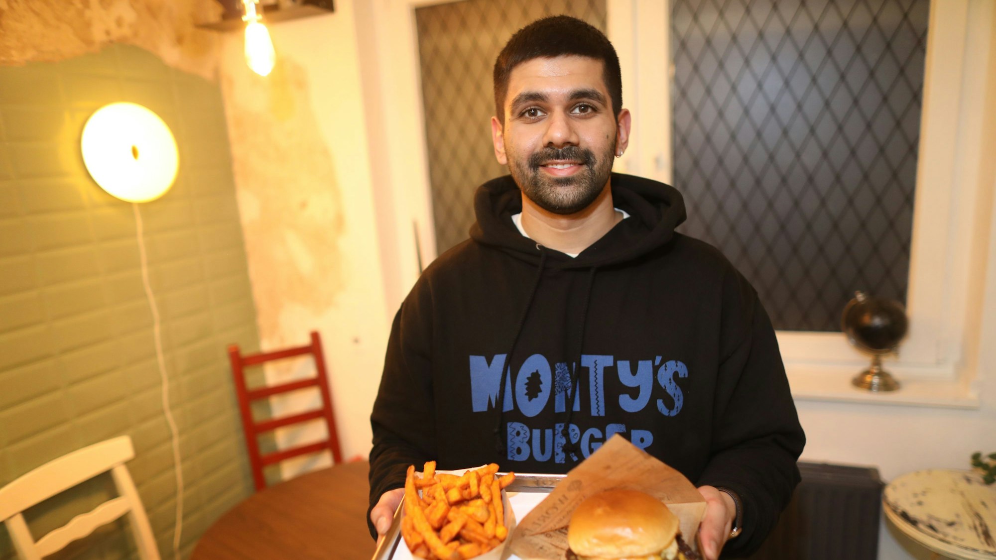 Inhaber Mandip Singh ist mti einem Tablett voll Burger und Fritten zu sehen.