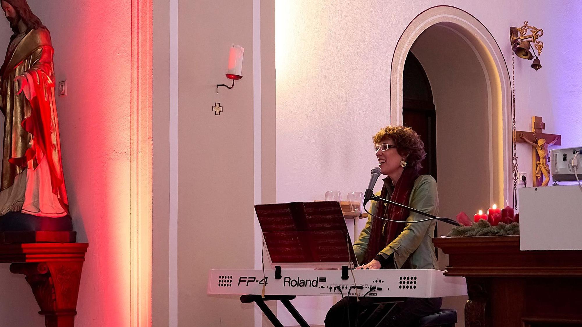Die Kölner Sängerin Kathrin Eigendorf sitzt in einer Kirche an einem weißen E-Piano und singt in ein Mikrofon.