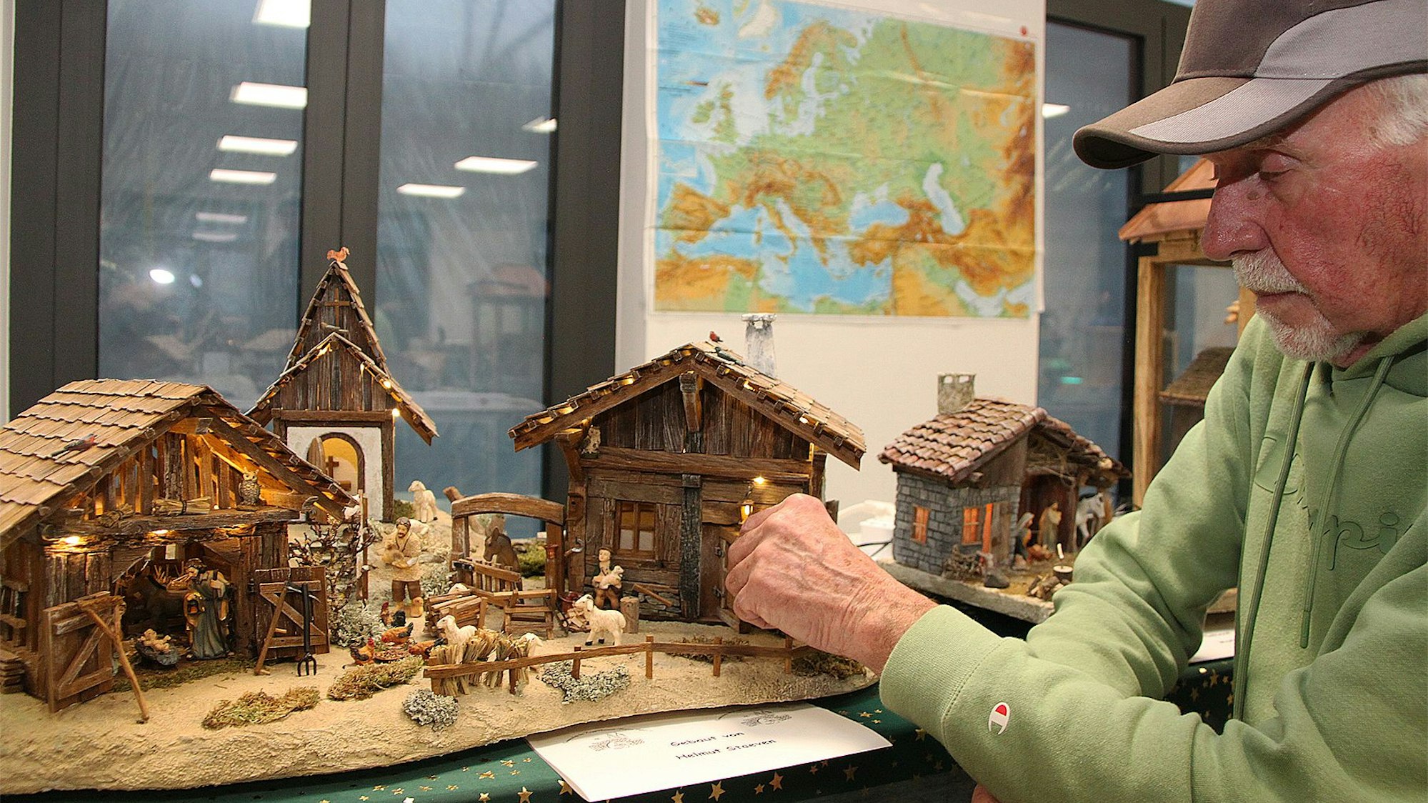 Ein Mann steht an einer auf einem Tisch aufgebauten Krippendarstellung.