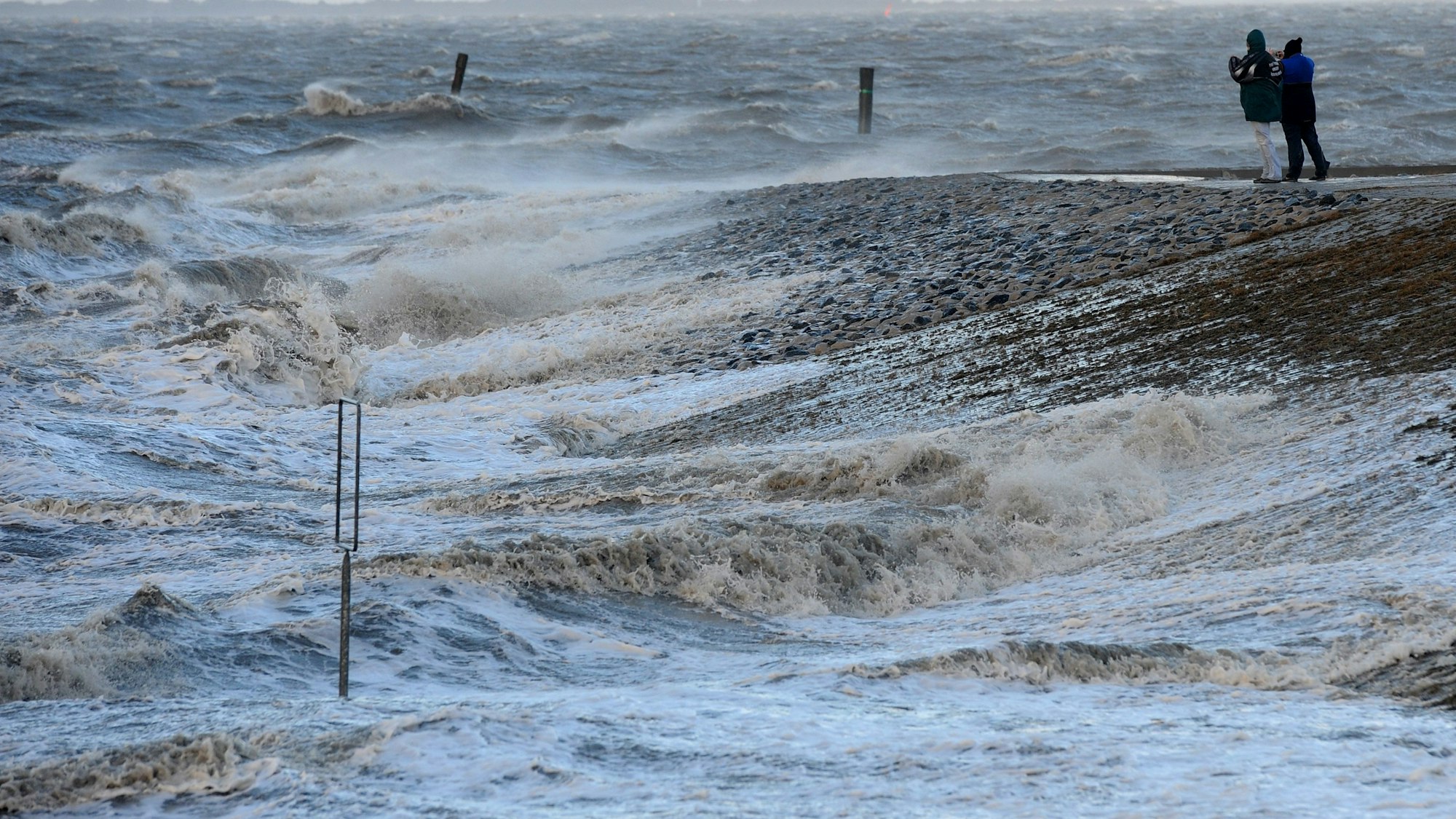 ARCHIV - Ein Paar schaut am 06.12.2013 bei Sturmflut am Hafen in Neuharlingersiel (Niedersachsen) auf die heranrollenden Wellen. Am 29.9. treffen sich auf einer Konferenz in Bremen Experten, um über Veränderungen durch den Klimawandel in der Nordsee-Region zu diskutieren. Foto: Ingo Wagner/dpa (zu lni vom 27.09.2015) +++(c) dpa - Bildfunk+++