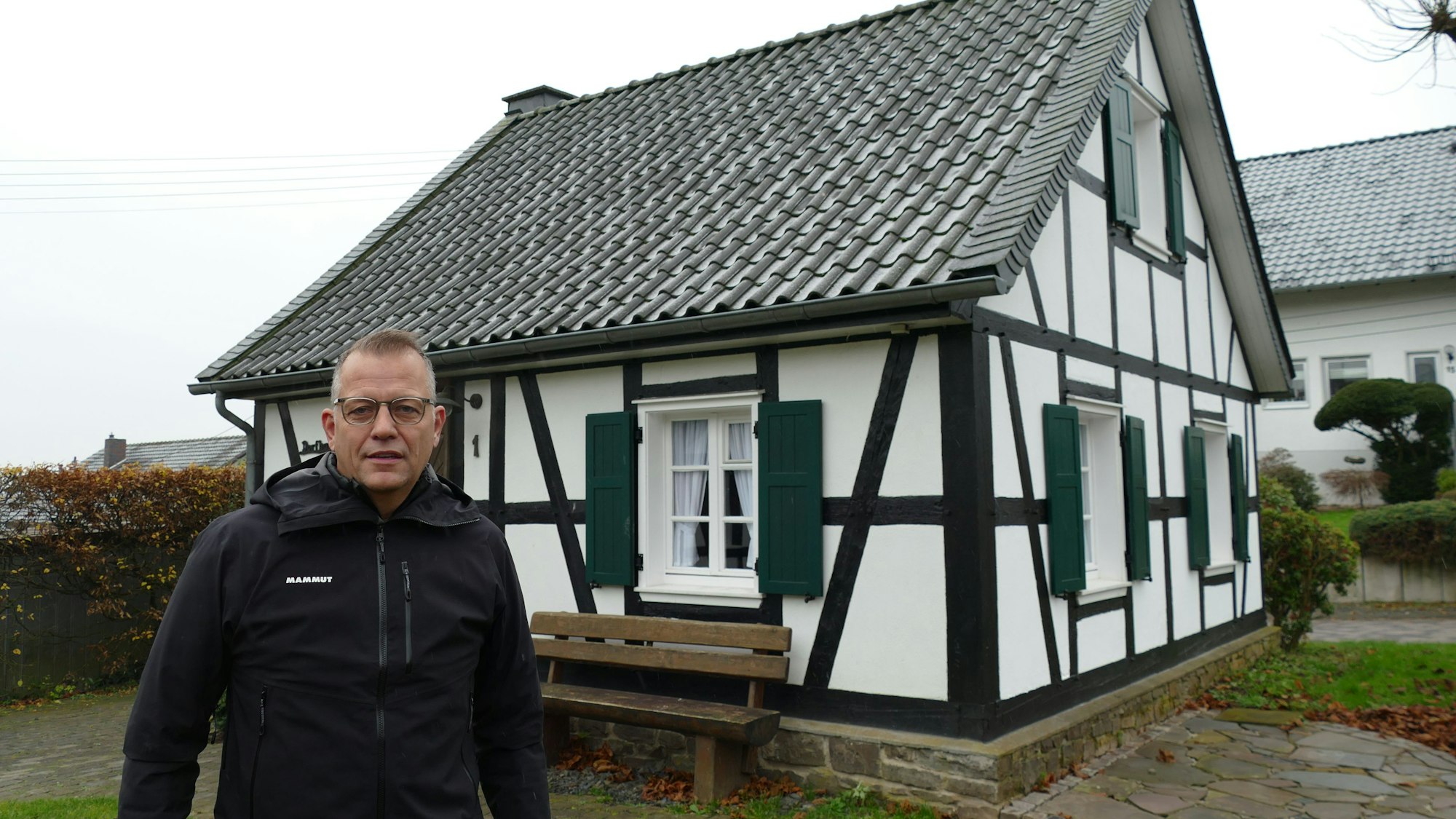 Ein Mann steht vor einem kleinen Fachwerkhaus.