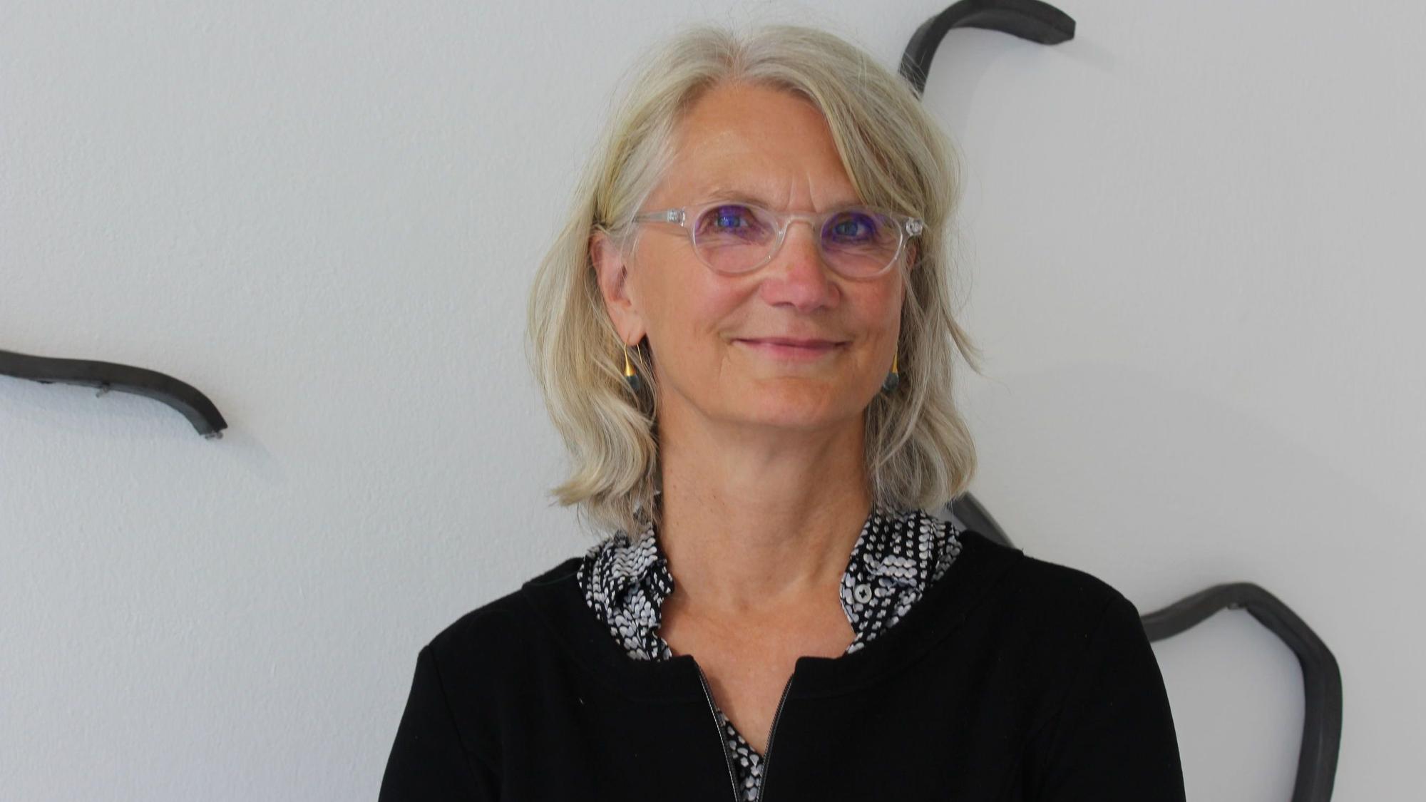 Eine Frau mit blonden Haaren und einer Brille schaut in die Kamera.