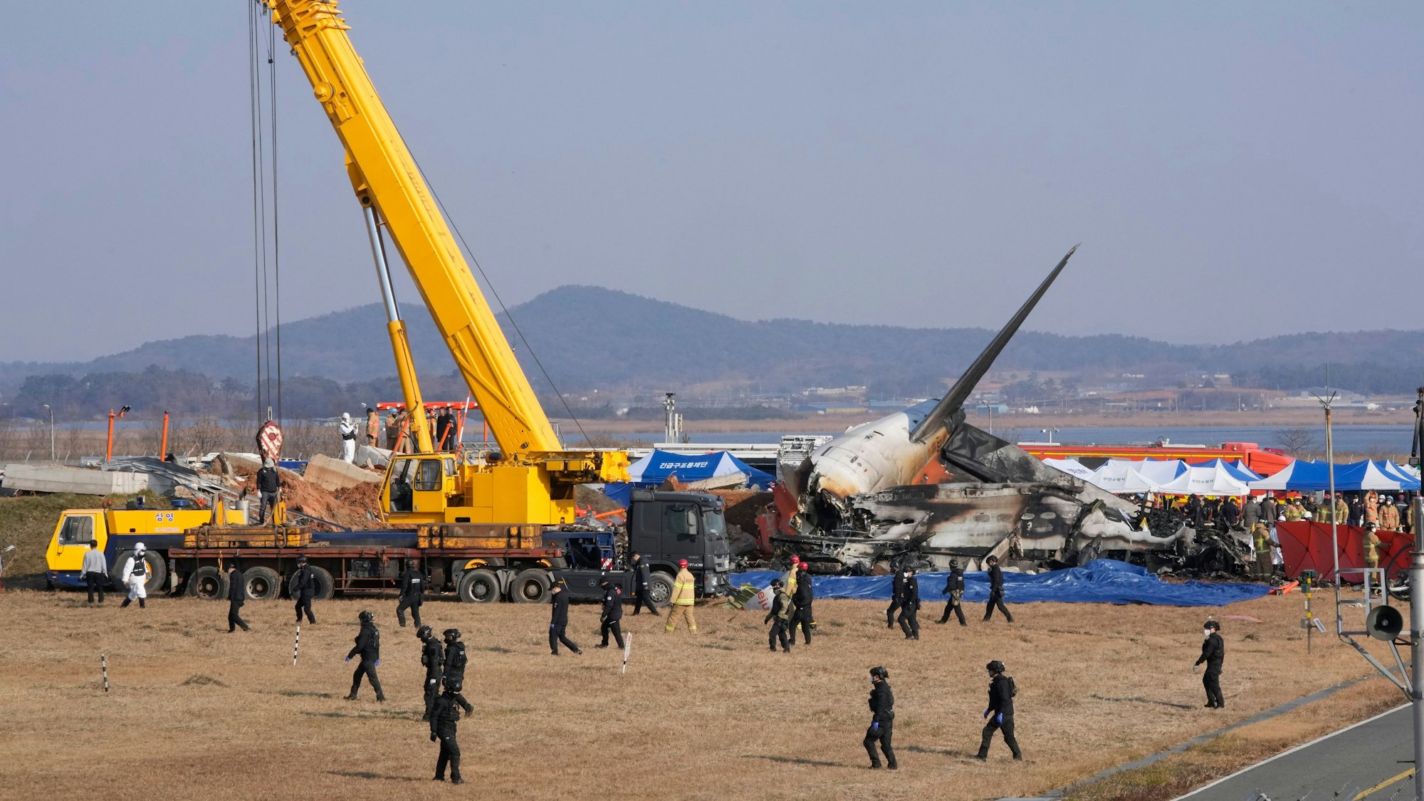 Feuerwehrleute und Mitglieder eines Rettungsteams arbeiten in der Nähe des Wracks eines Passagierflugzeugs am Muan International Airport.