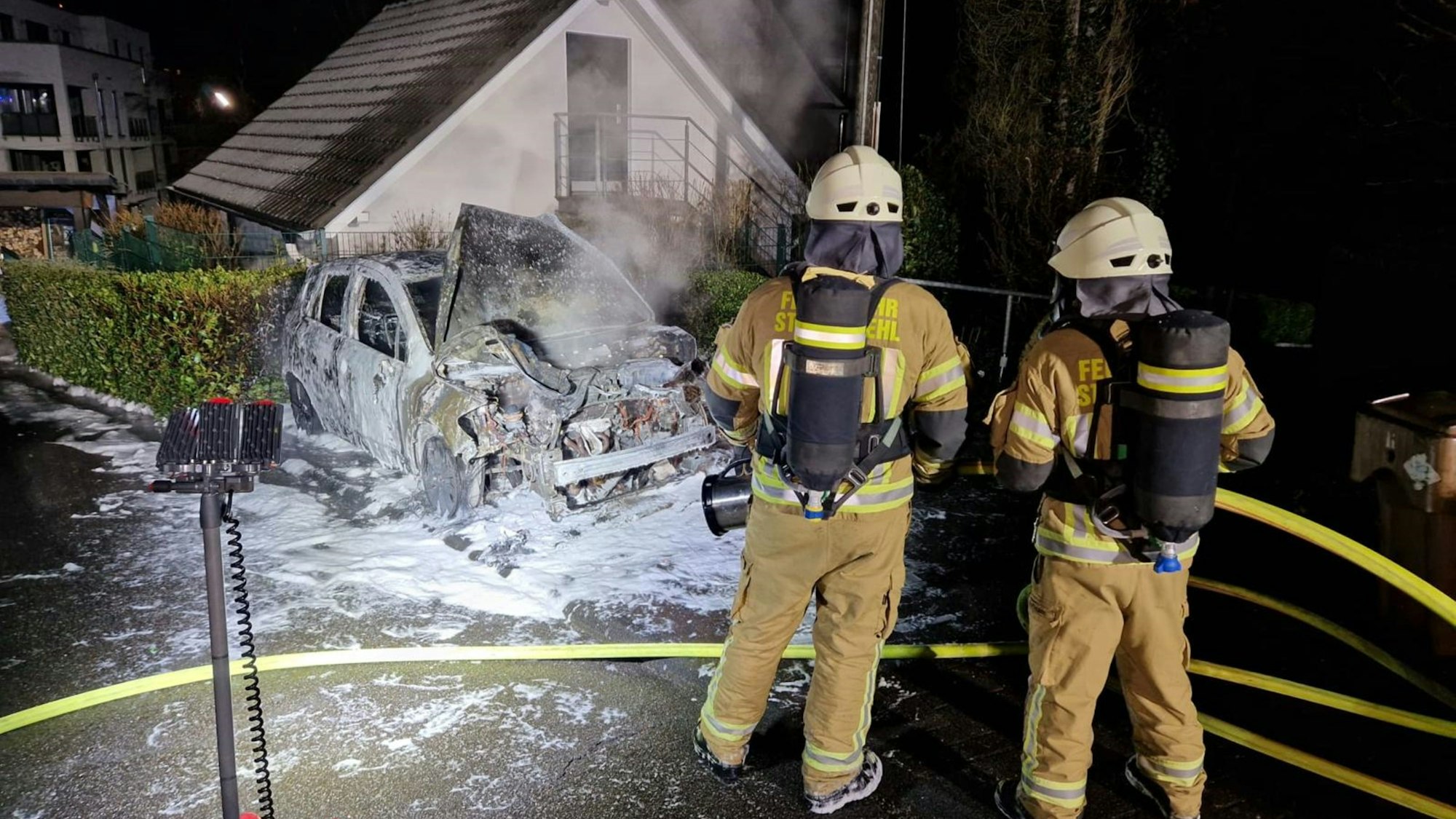 Das Foto zeigt zwei Feuerwehrleute vor dem ausgebrannten Pkw.