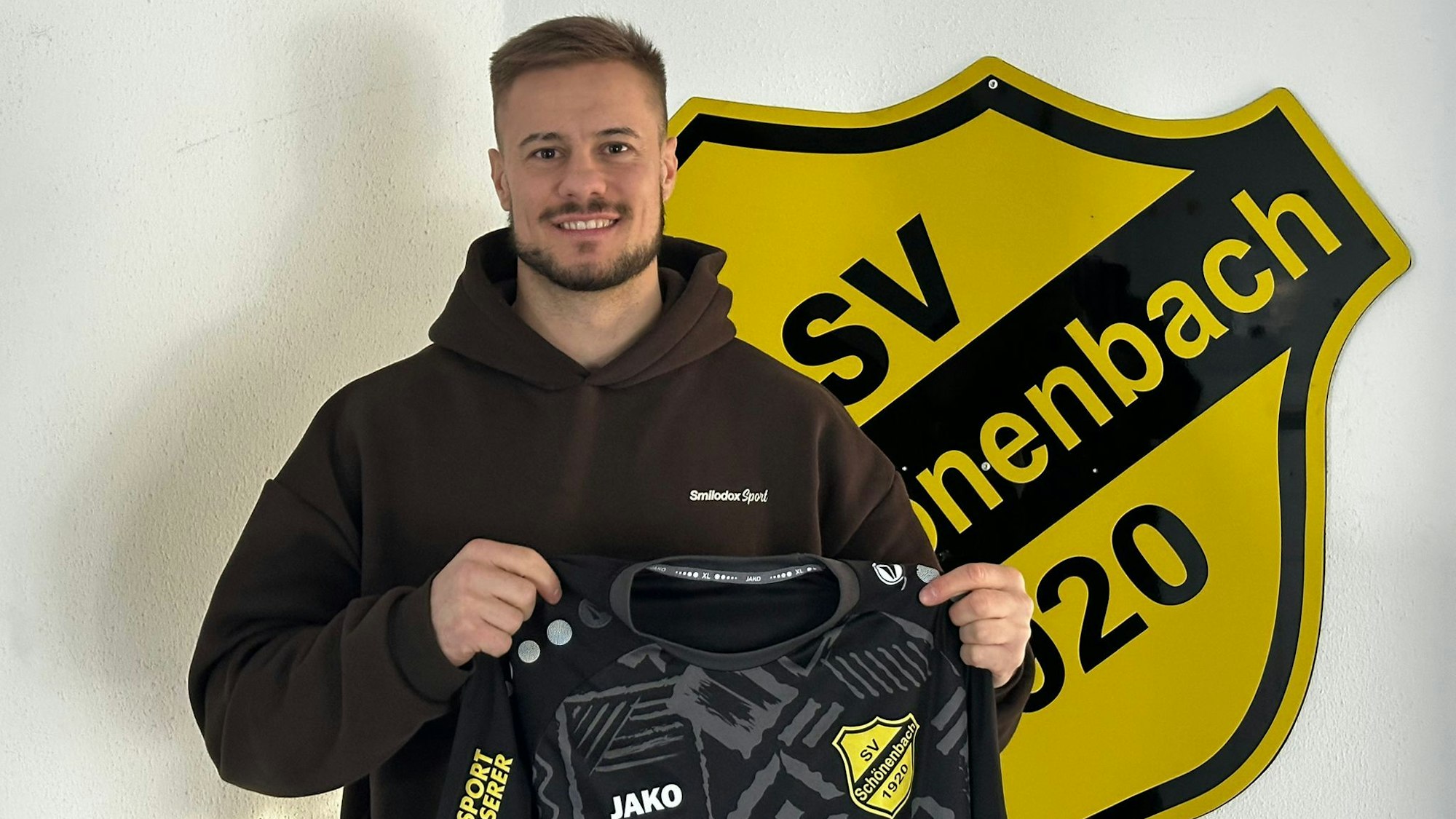 Neuzugang Sven Wurm vor dem Vereinsemblem mit dem Trikot den Händen.