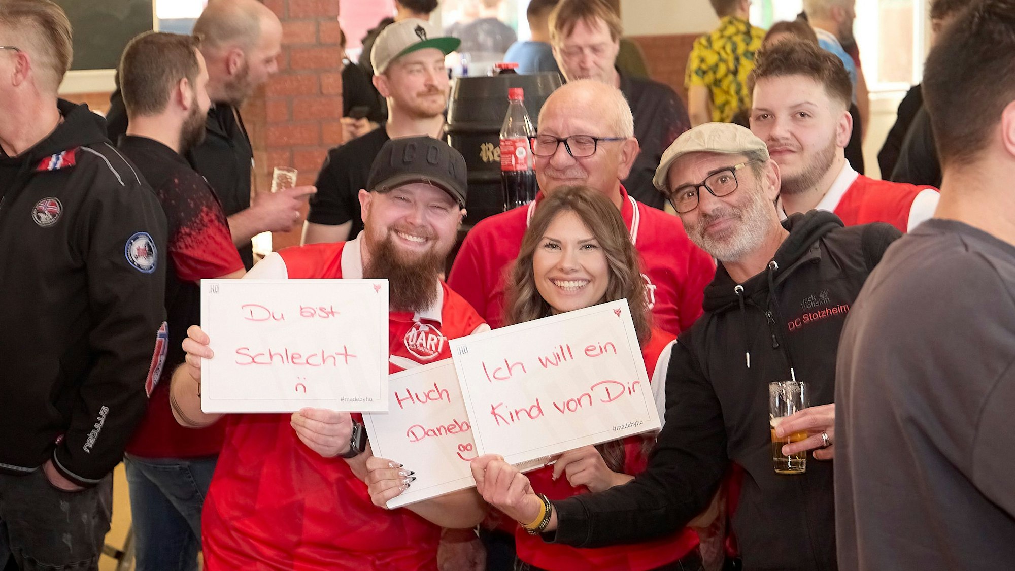 Für Stimmung wie im Ally Pally sorgten die Fans auch in der Eifel. Drei von ihnen halten beschriebene Schilder in die Kamera.
