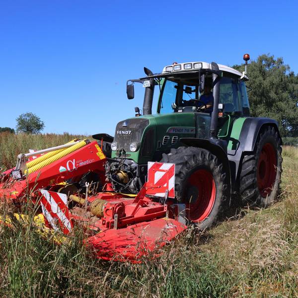 Ein Traktor mäht eine Wiese mit hohem Gras.