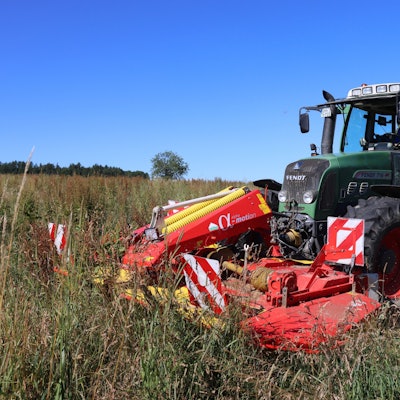 Ein Traktor mäht eine Wiese mit hohem Gras.