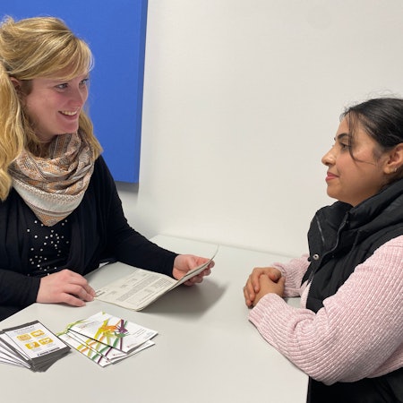 Nora Habeth-Baumgarten und Elmaz Arab sitzen sich gegenüber. Papiere und Broschüren liegen zwischen ihnen auf einem Tisch.