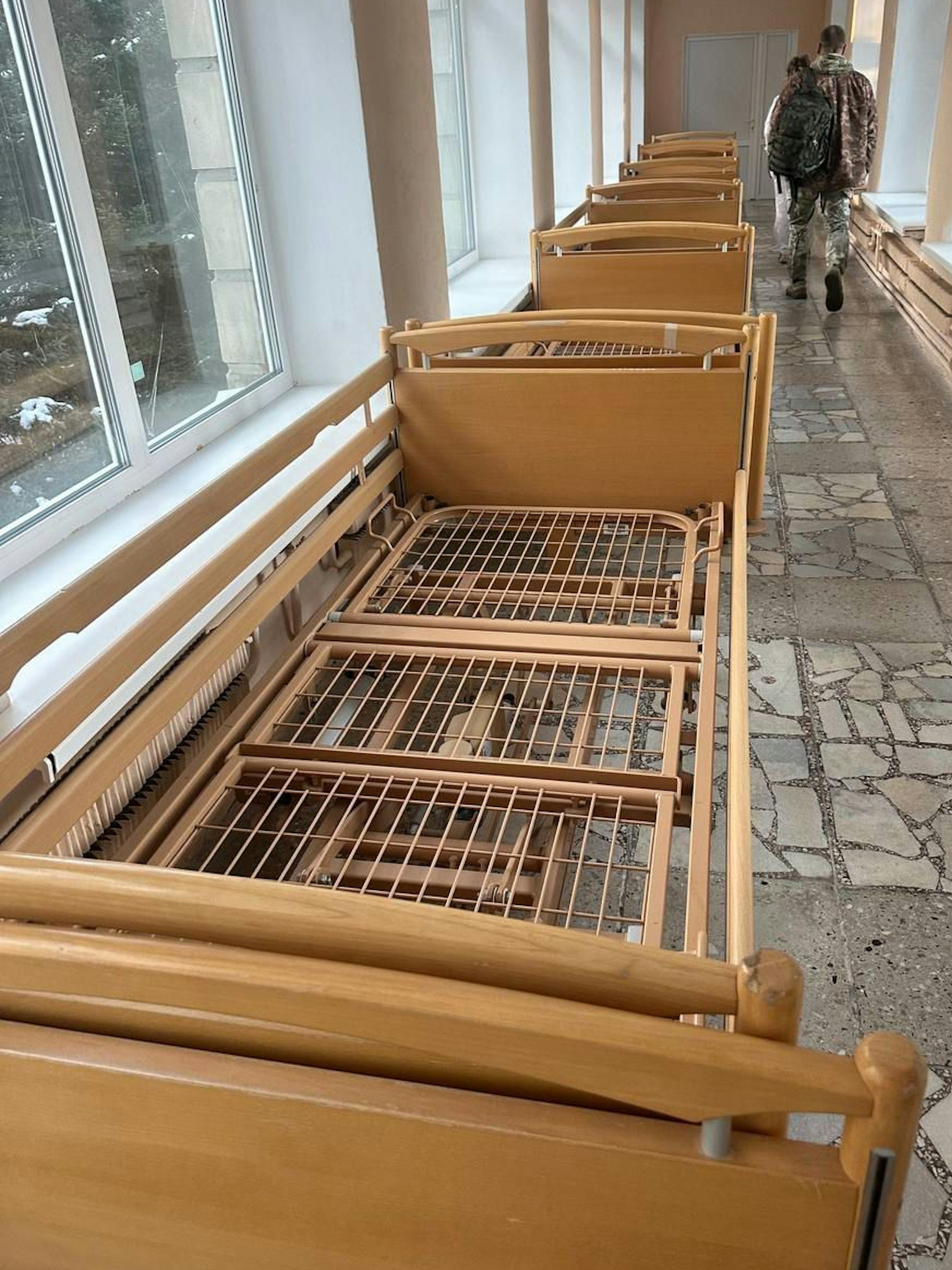 In einem Krankenhausgang stehen mehrere hölzerne Betten.