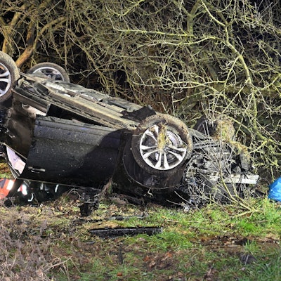 Ein schwarzes Auto liegt auf dem Dach und völlig zerbeult in einem Busch.