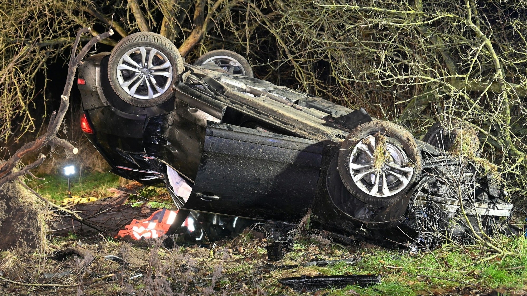 Ein schwarzes Auto liegt auf dem Dach und völlig zerbeult in einem Busch.
