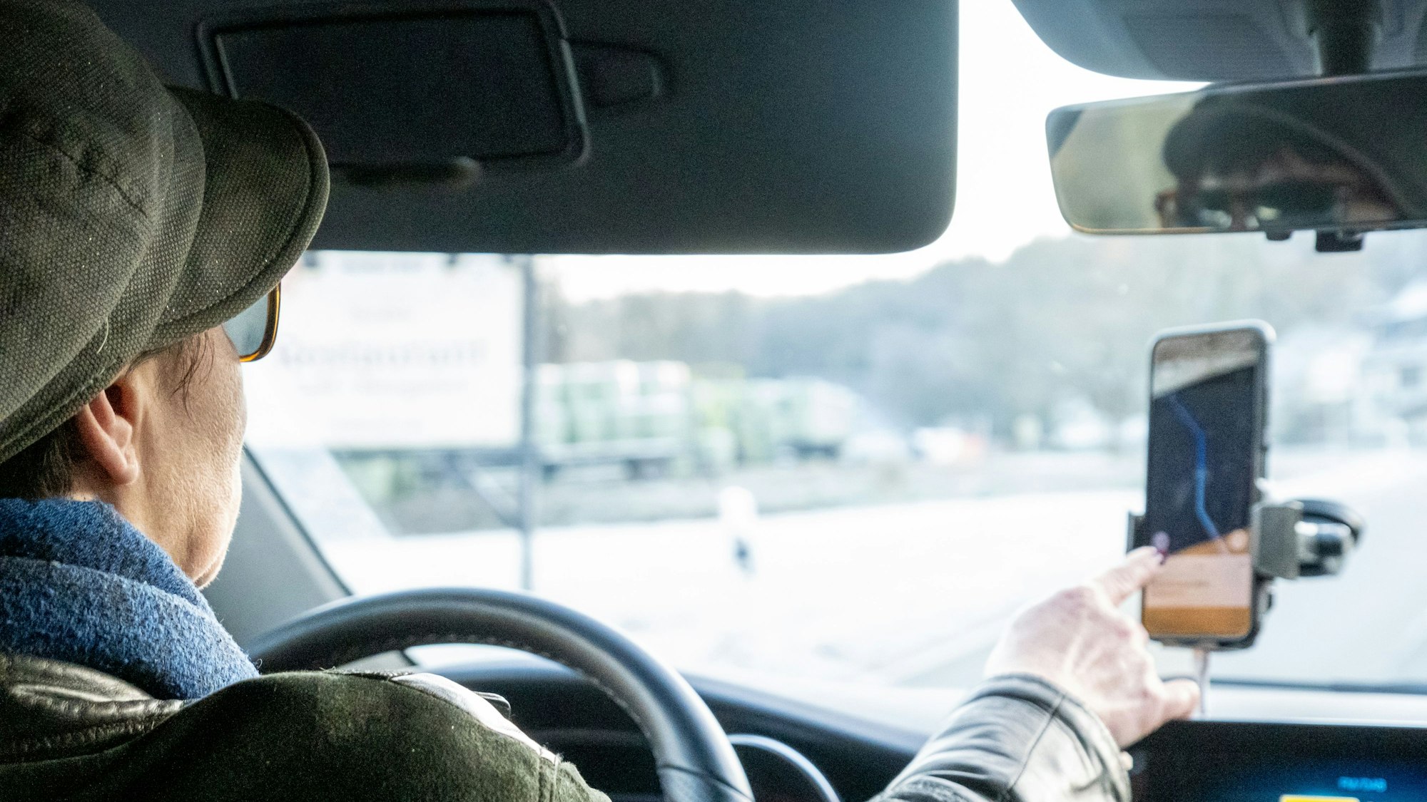 Eine Frau sitzt am Lenkrad eines Taxis und stellt die Fahrt-App ein.