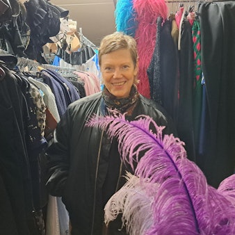 Eine Frau mit kurzen Haaren steht zwischen Kleiderstangen voller Kostüme.