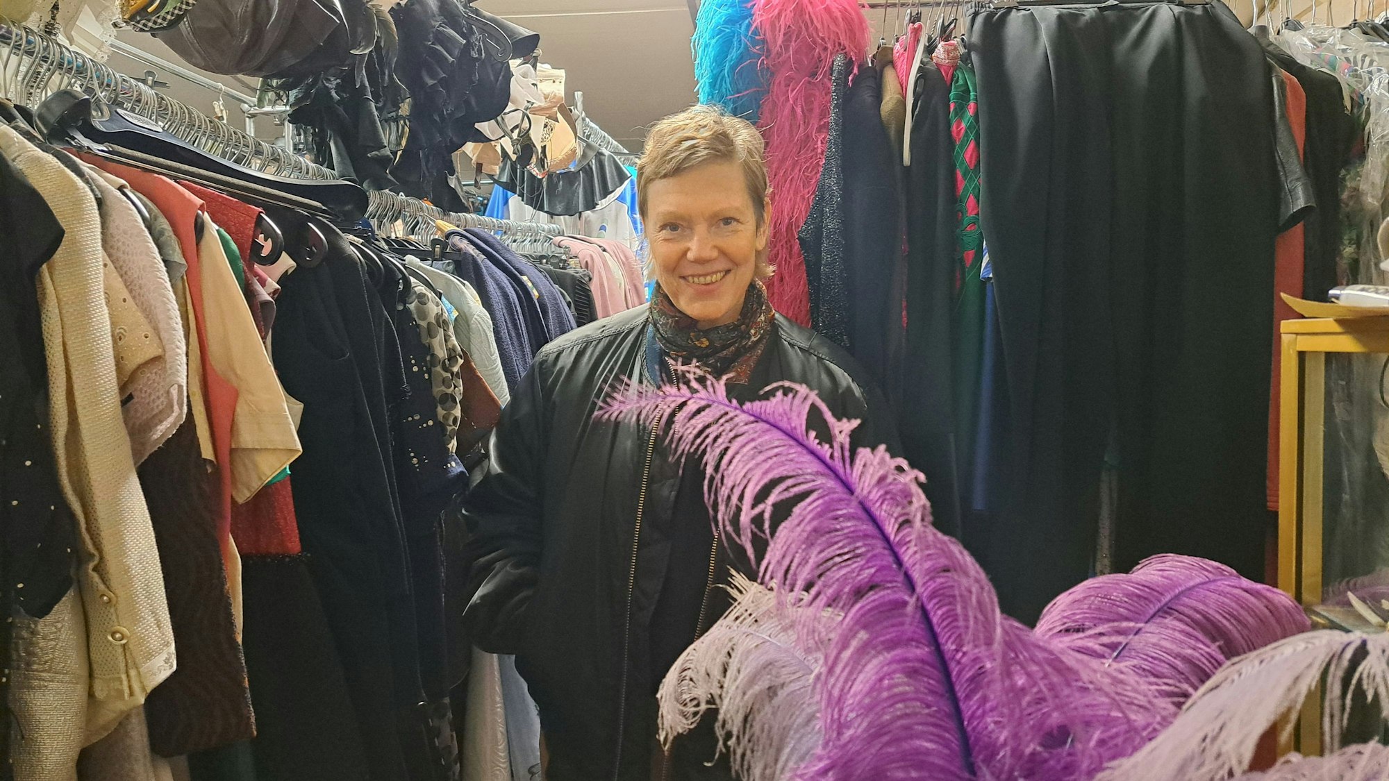 Eine Frau mit kurzen Haaren steht zwischen Kleiderstangen voller Kostüme.