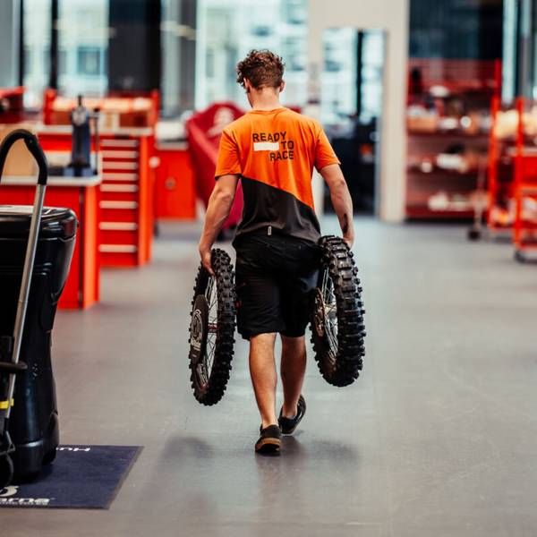Bild eines Mannes, der ein Paar Motorradreifen durch eine Halle trägt.