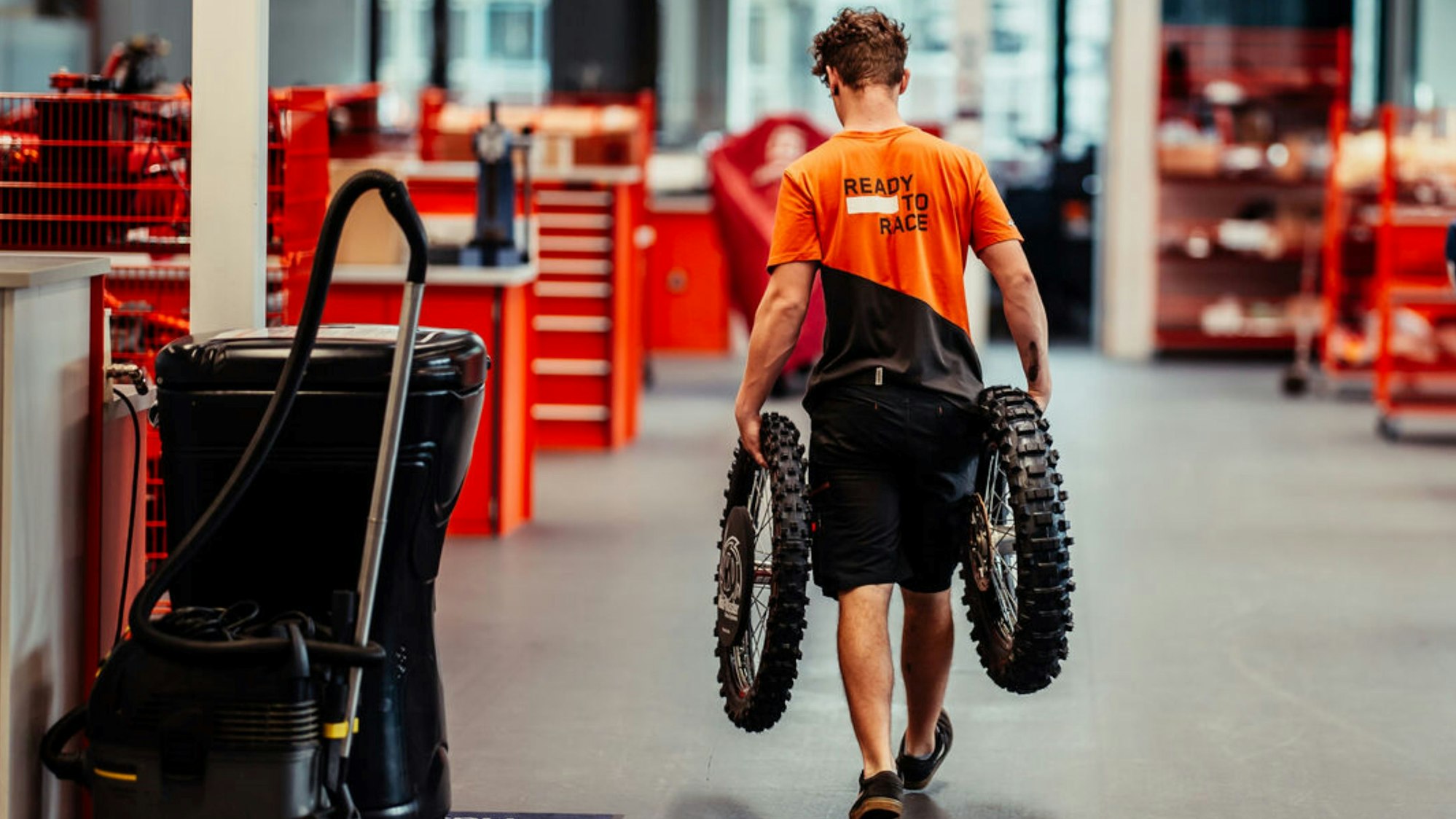 Bild eines Mannes, der ein Paar Motorradreifen durch eine Halle trägt.
