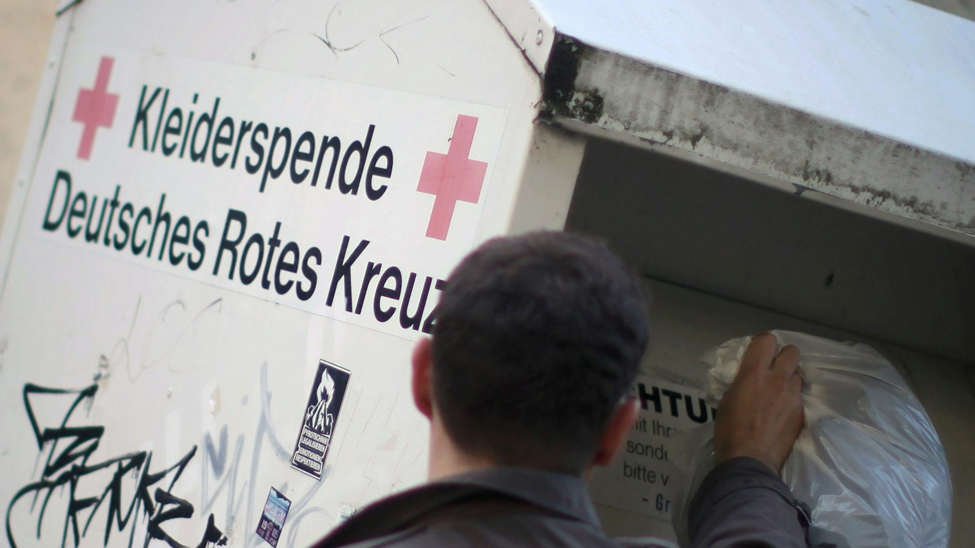 Ein Mann wirft Altkleider in einen Altkleider-Container.