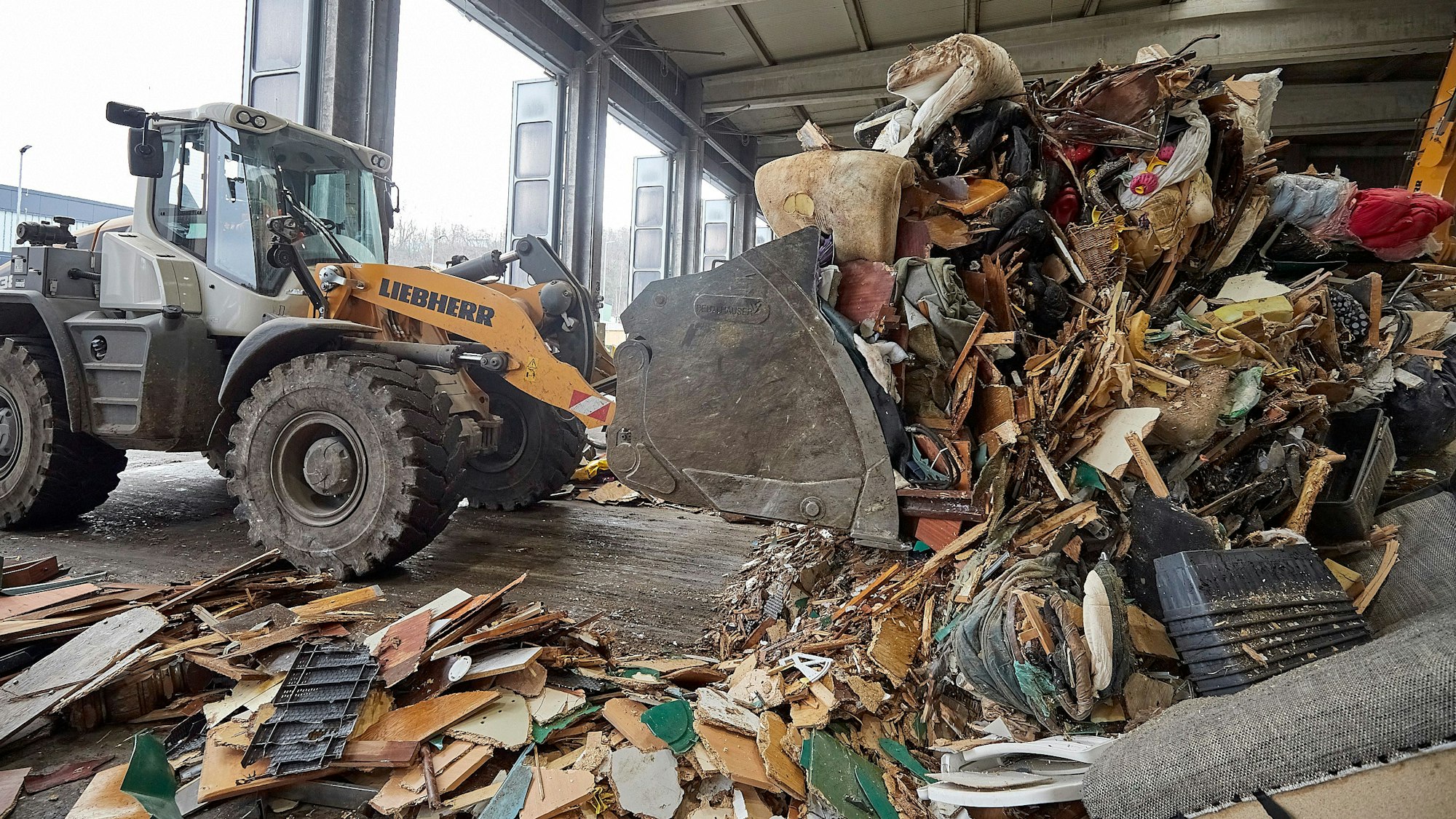 Mit einem Bagger wird im Abfallwirtschaftszentrum des Kreises Euskirchen in einer Halle Müll zusammengeschoben.