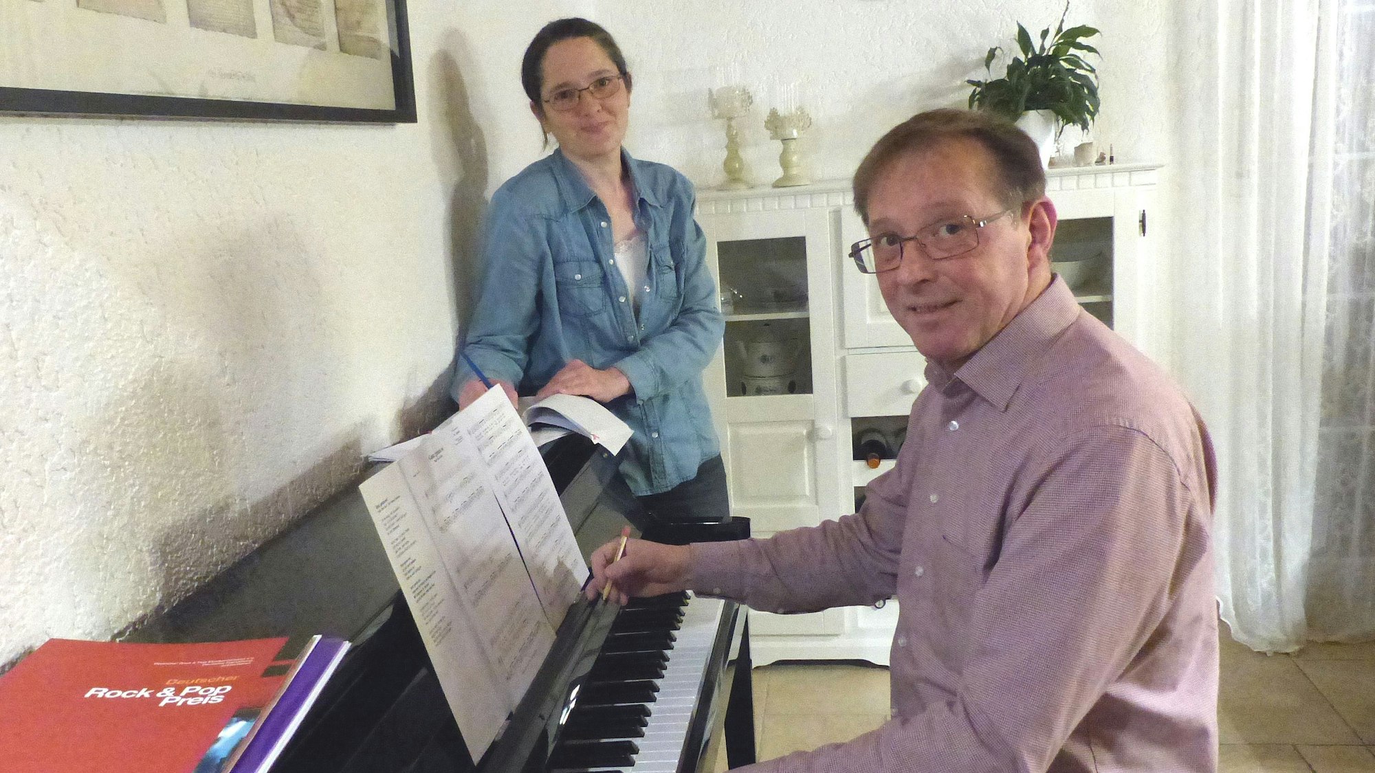 Ein Mann sitzt am Klavier, dahinter steht eine Frau.