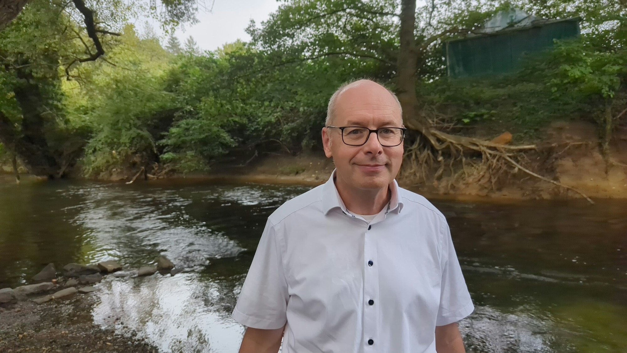 Holger Schüttrumpf steht lächelnd vor einem kleinen Fluss.