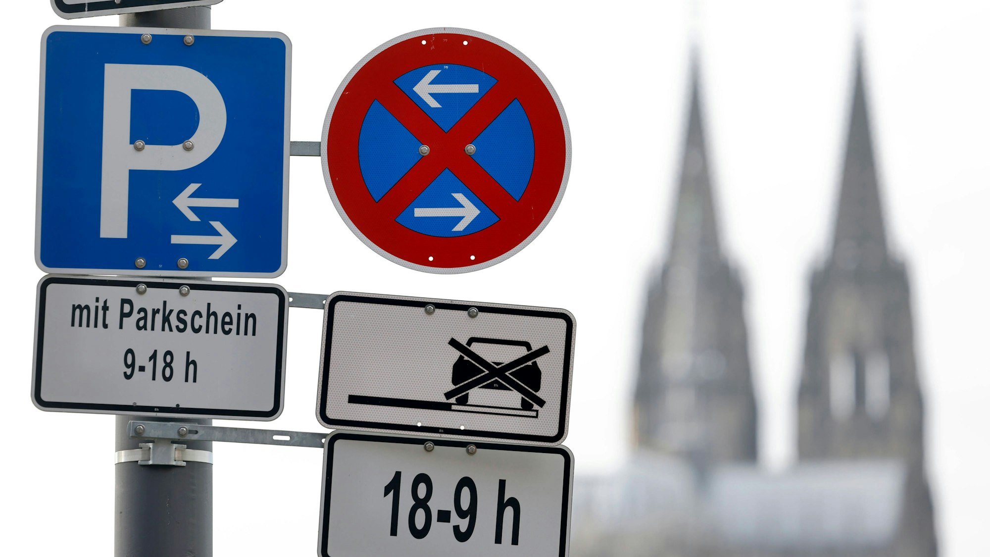 Die Parkplatzsuche in Köln stellt Autofahrer des öfteren vor große Herausforderungen. Im Bild ein Parkverbotsschild mit Parkplatzschild am Deutzer Rheinufer, im Hintergrund der Kölner Dom.