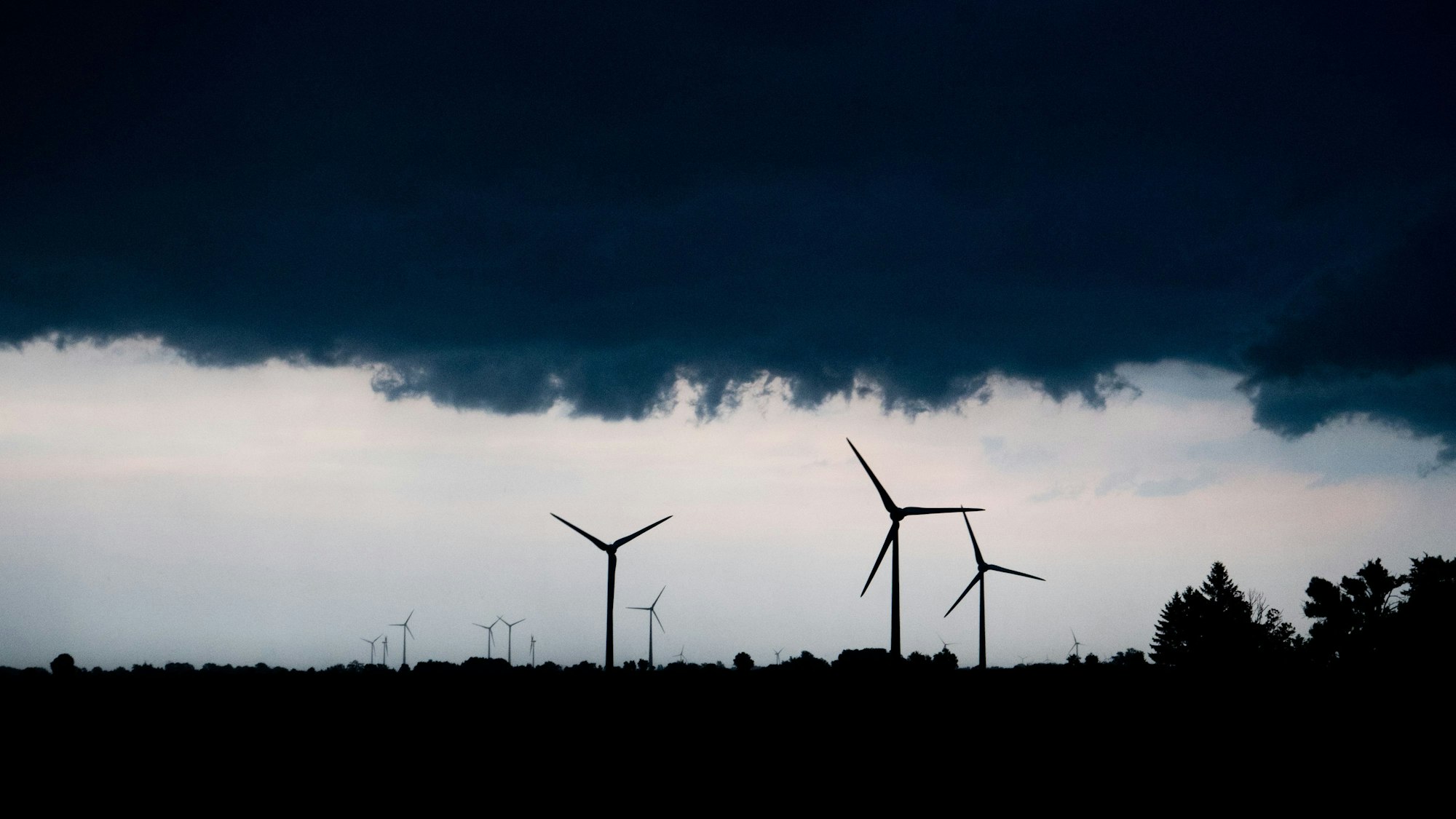 Mehrere Windräder ragen in den Himmel, der von Regenwolken verdunkelt ist.