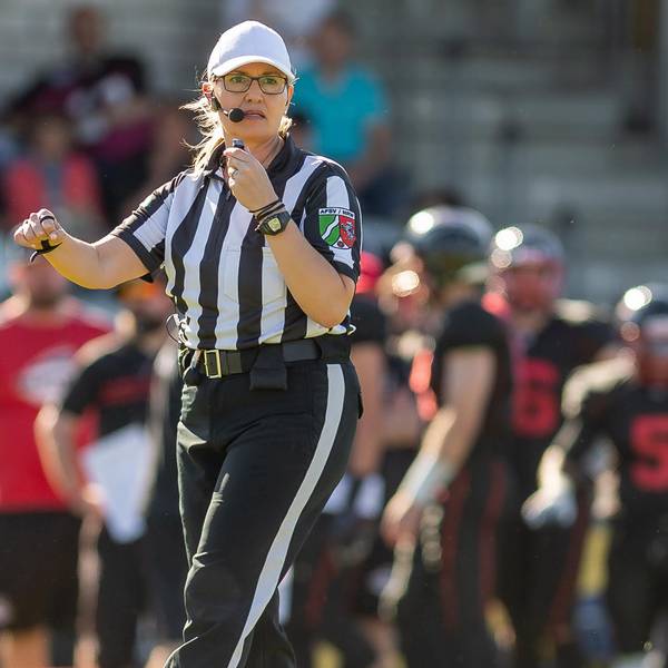 Gudrun Bogman trägt das schwarz-weiß-gestreifte Schiedsrichteroutfit, während sie ein Footballspiel pfeift.