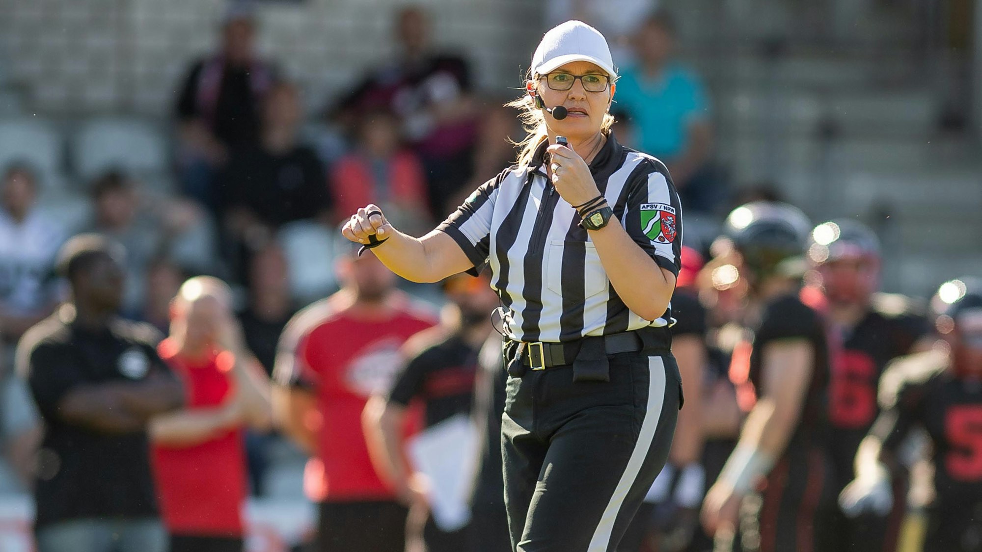 Gudrun Bogman trägt das schwarz-weiß-gestreifte Schiedsrichteroutfit, während sie ein Footballspiel pfeift.