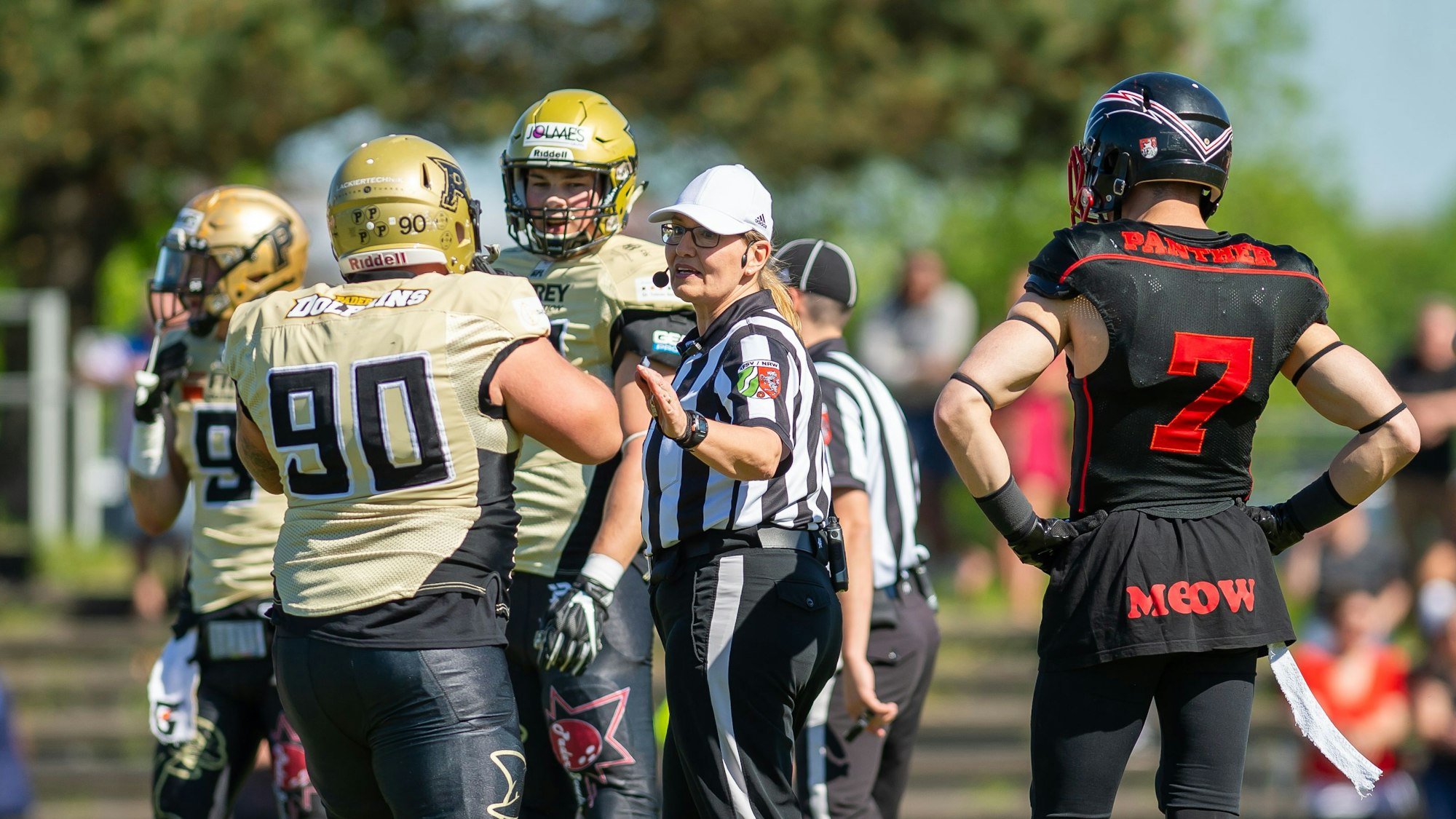 Während eines Footballspiels redet Schiedsrichterin Gudrun Bogman mit Spielern zweier Teams auf dem Feld.