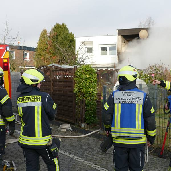 Feuerwehrleute stehen auf der Rückseite des brennenden Hauses.