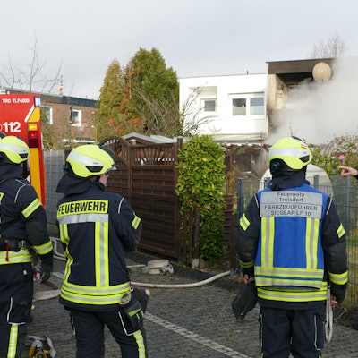 Feuerwehrleute stehen auf der Rückseite des brennenden Hauses.