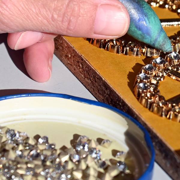 Nahaufnahme von einer Hand, die Glitzersteinchen auf einen Orden klebt.