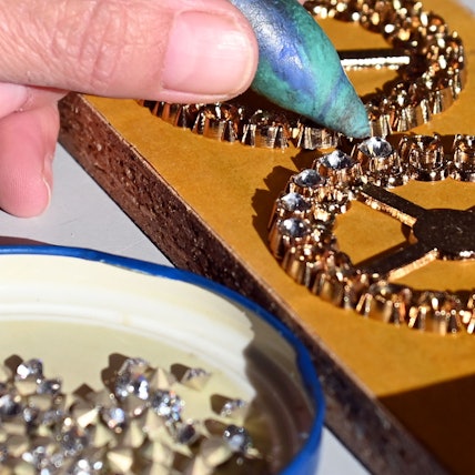 Nahaufnahme von einer Hand, die Glitzersteinchen auf einen Orden klebt.