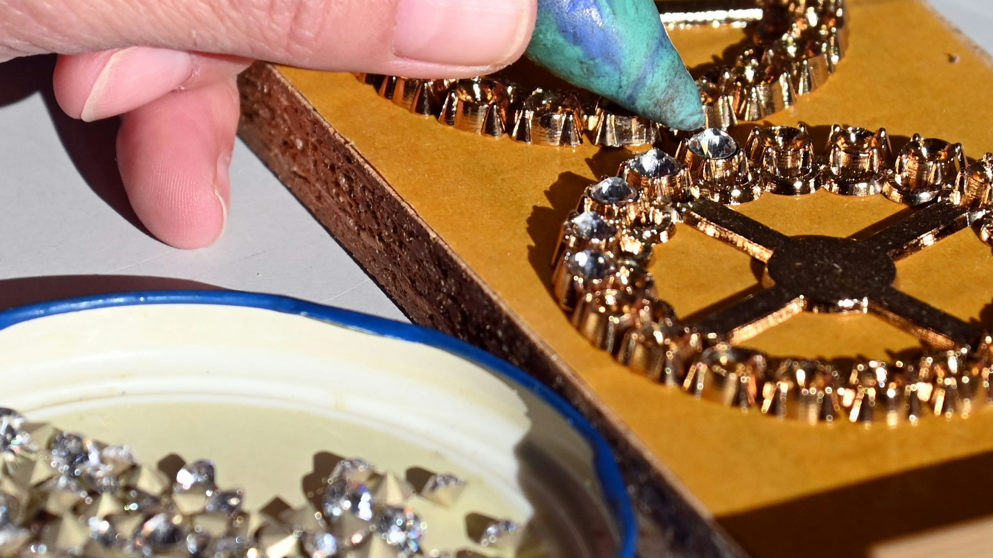 Nahaufnahme von einer Hand, die Glitzersteinchen auf einen Orden klebt.