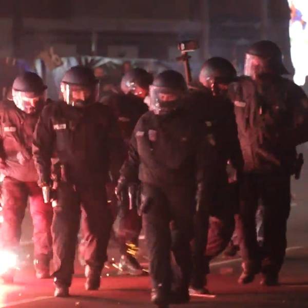 Einsatzkräfte der Polizei stehen in der Silvesternacht zwischen brennendem Feuerwerk.