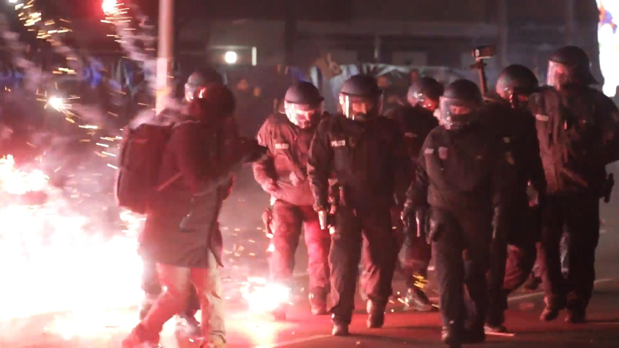 Einsatzkräfte der Polizei stehen in der Silvesternacht zwischen brennendem Feuerwerk.