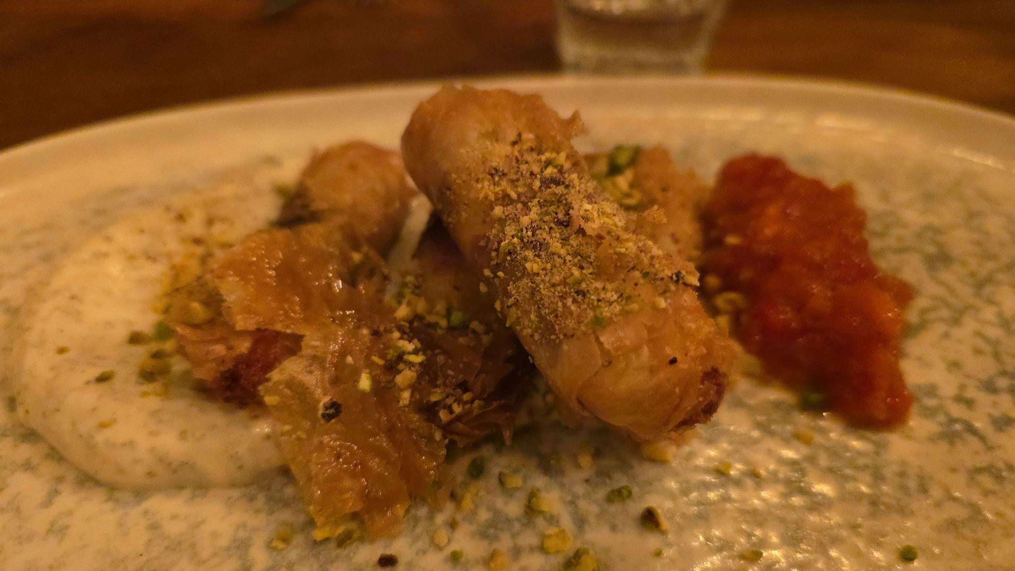 Baklava-Röllchen sind auf einem Teller mit Joghurt-Sauce zu sehen.