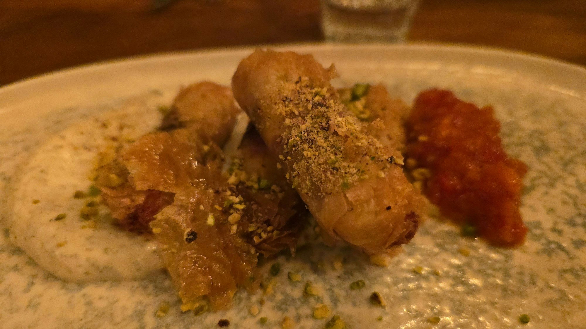 Baklava-Röllchen sind auf einem Teller mit Joghurt-Sauce zu sehen.