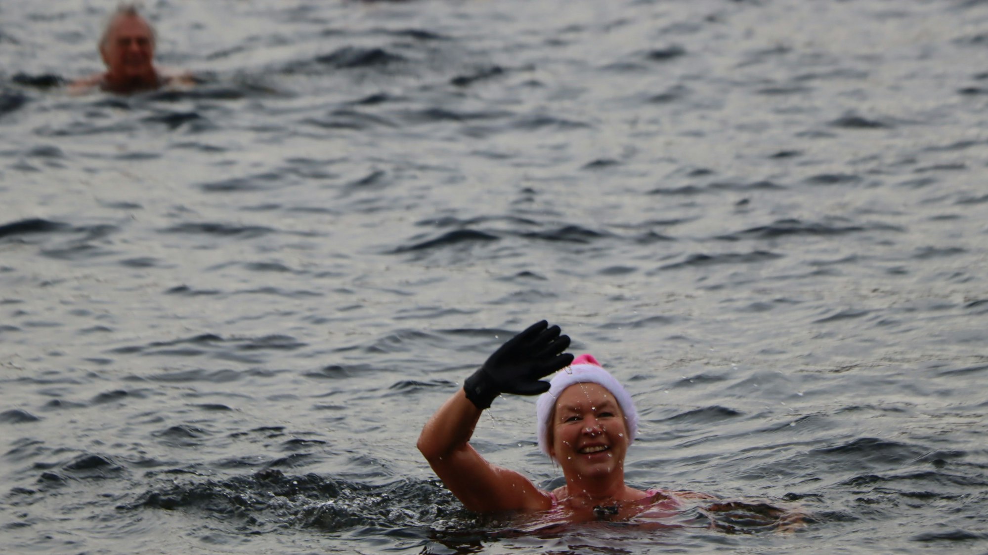 Auf dem Bild ist eine Frau mit Nikolausmütze zu sehen, die im See schwimmt und winkt.