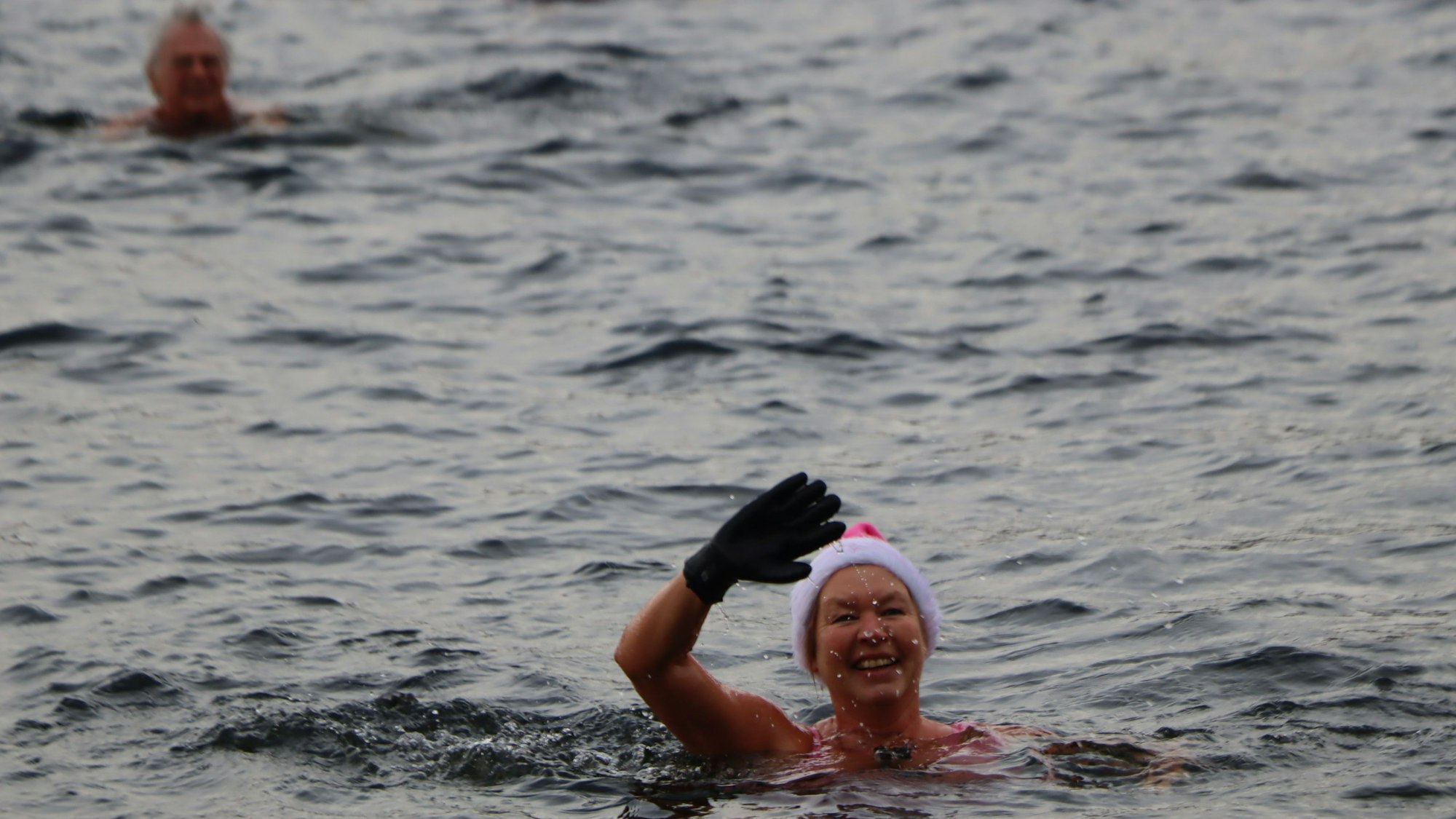 Auf dem Bild ist eine Frau mit Nikolausmütze zu sehen, die im See schwimmt und winkt.