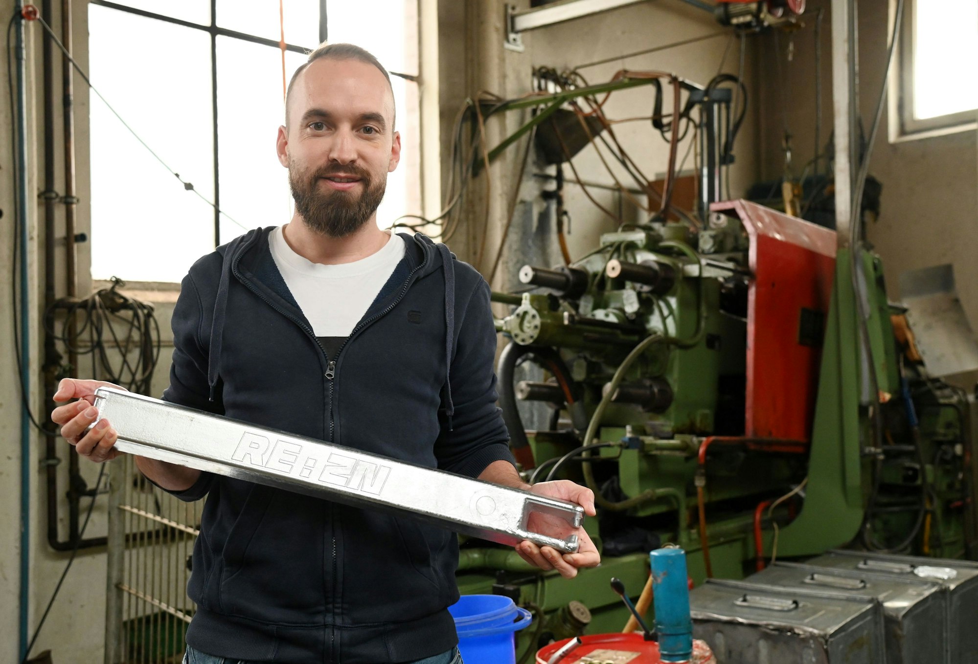Sascha Bley mit Alu-Zink-Legierung, hinter ihm eine große Maschine.