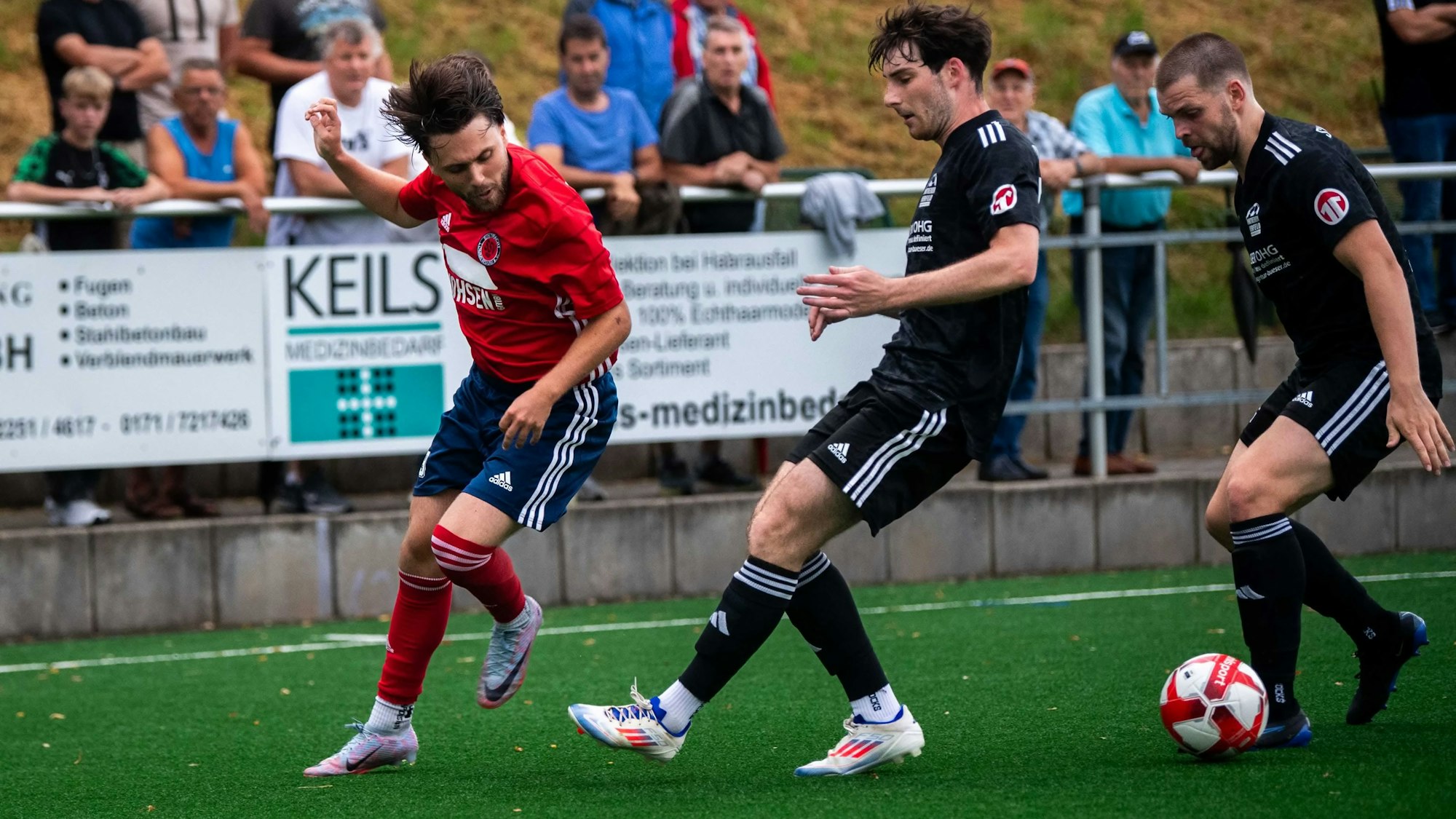Das Bild zeigt den Lommersumer Fußballer im Duell mit zwei Gegenspielern.