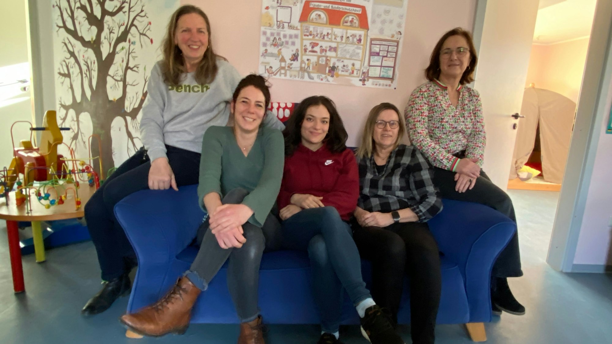 Fünf Frauen sitzen im Schutzhaus auf dem Sofa, hinter ihnen hängt ein Plakat.