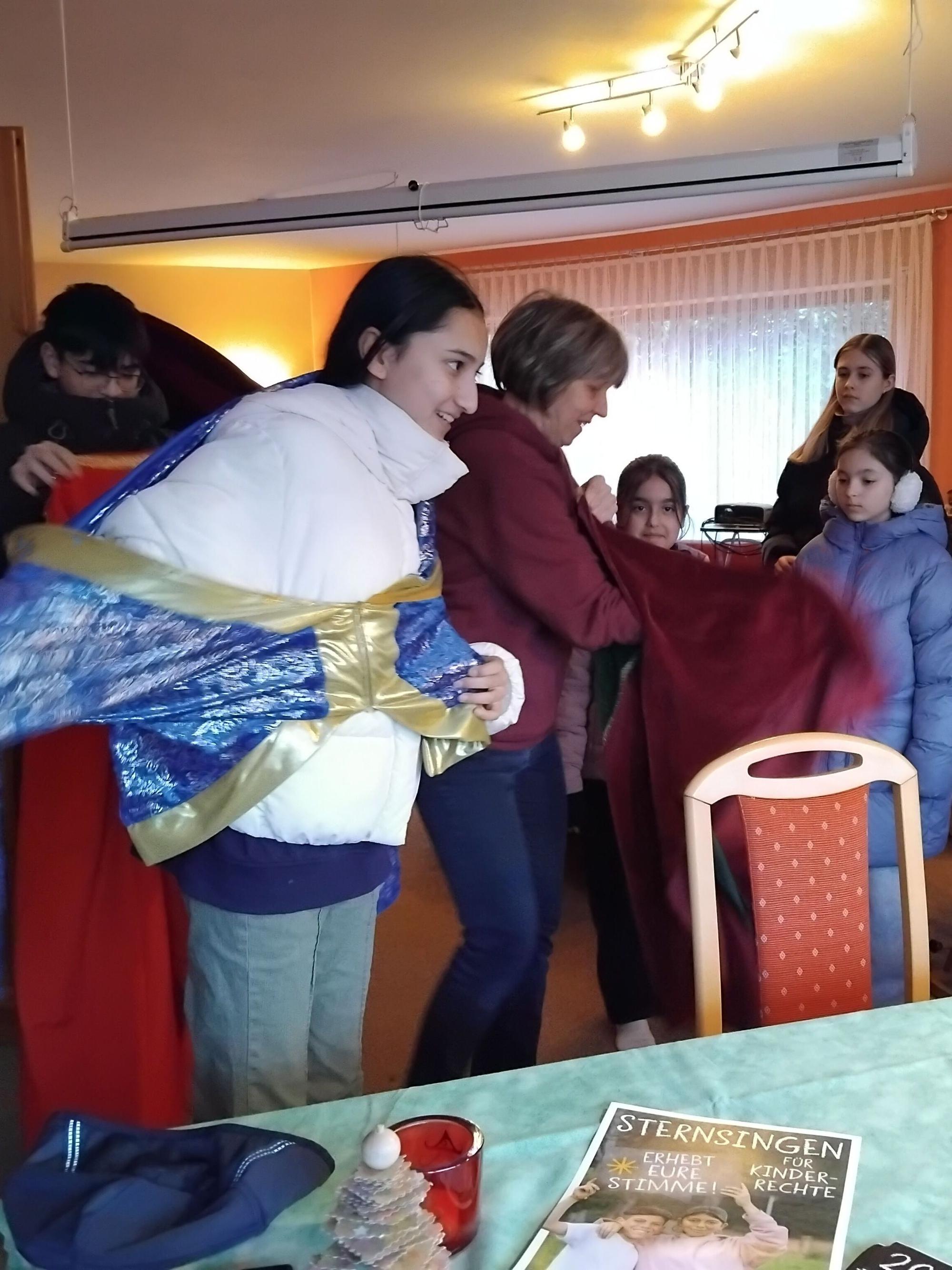 Kinder verkleiden sich als Heilige Drei Könige, eine Frau hilft