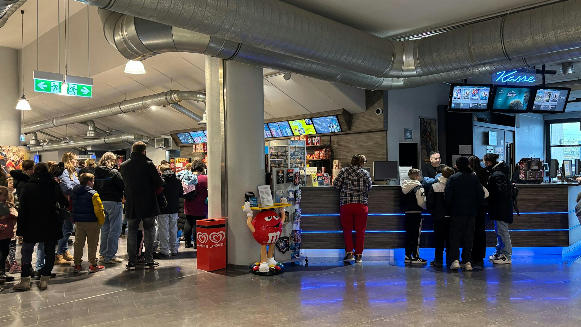 Der Eingangsbereich eines Kinos: Einige Menschen stehen an der Kasse, noch mehr am Popcorn- und Getränkestand an.