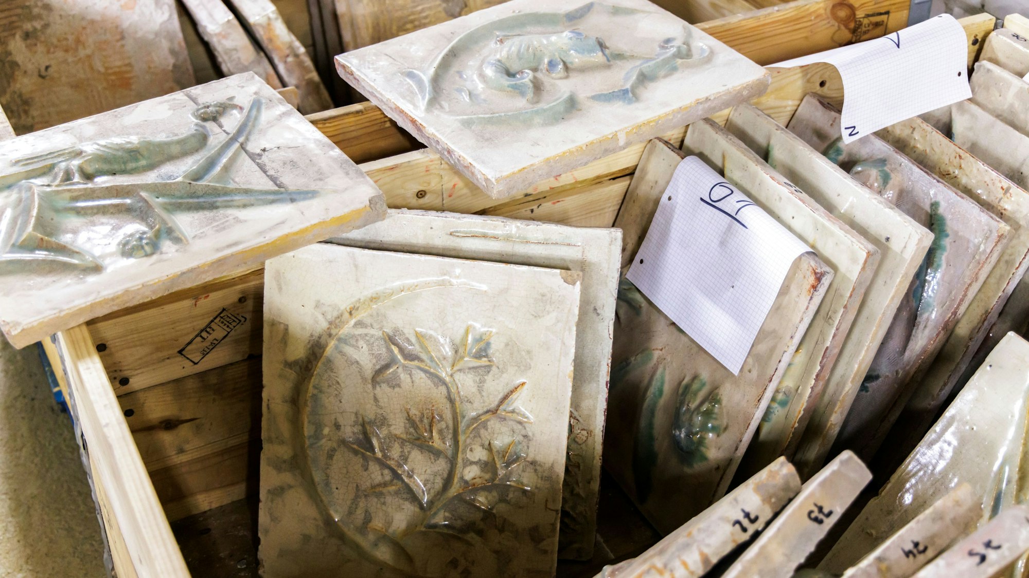 Auf dem Bild ist ein Teil der alten Fliesen in einer Holzkiste zu sehen.