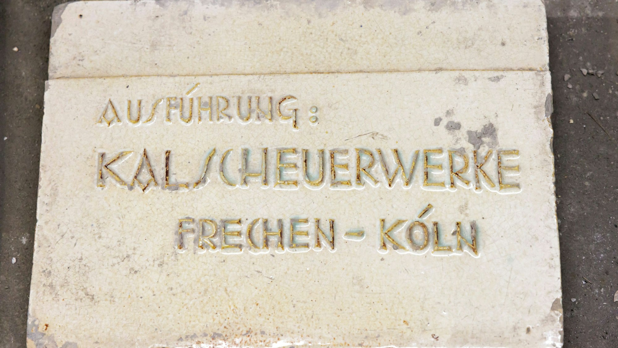 Auf dem Bild ist eine Fliese zu sehen, in die der Firmenname des Kalscheuerwerks geschrieben ist.