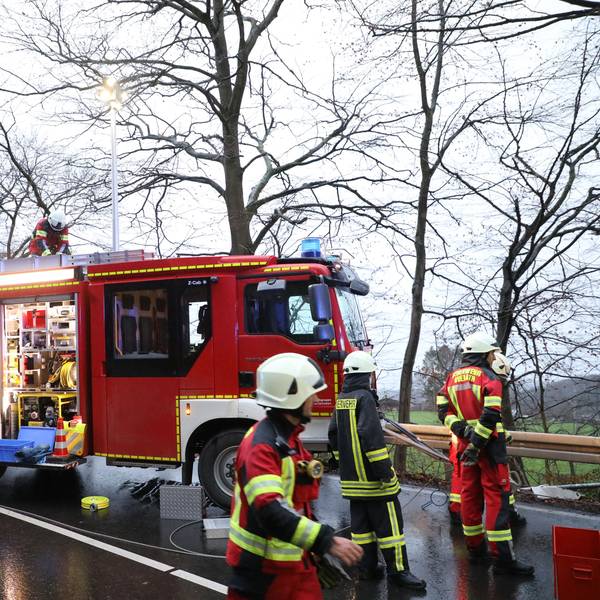 Ein Feuerwehrfahrzeug steht auf einer Landstraße, Feuerwehrmänner entnehmen dem Wagen Schläuche.