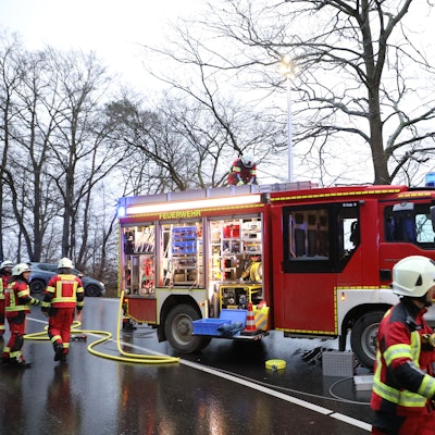 Ein Feuerwehrfahrzeug steht auf einer Landstraße, Feuerwehrmänner entnehmen dem Wagen Schläuche.